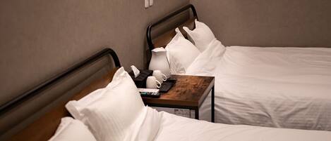 A hotel room with two beds, a wooden nightstand, and a wall-mounted power outlet.
