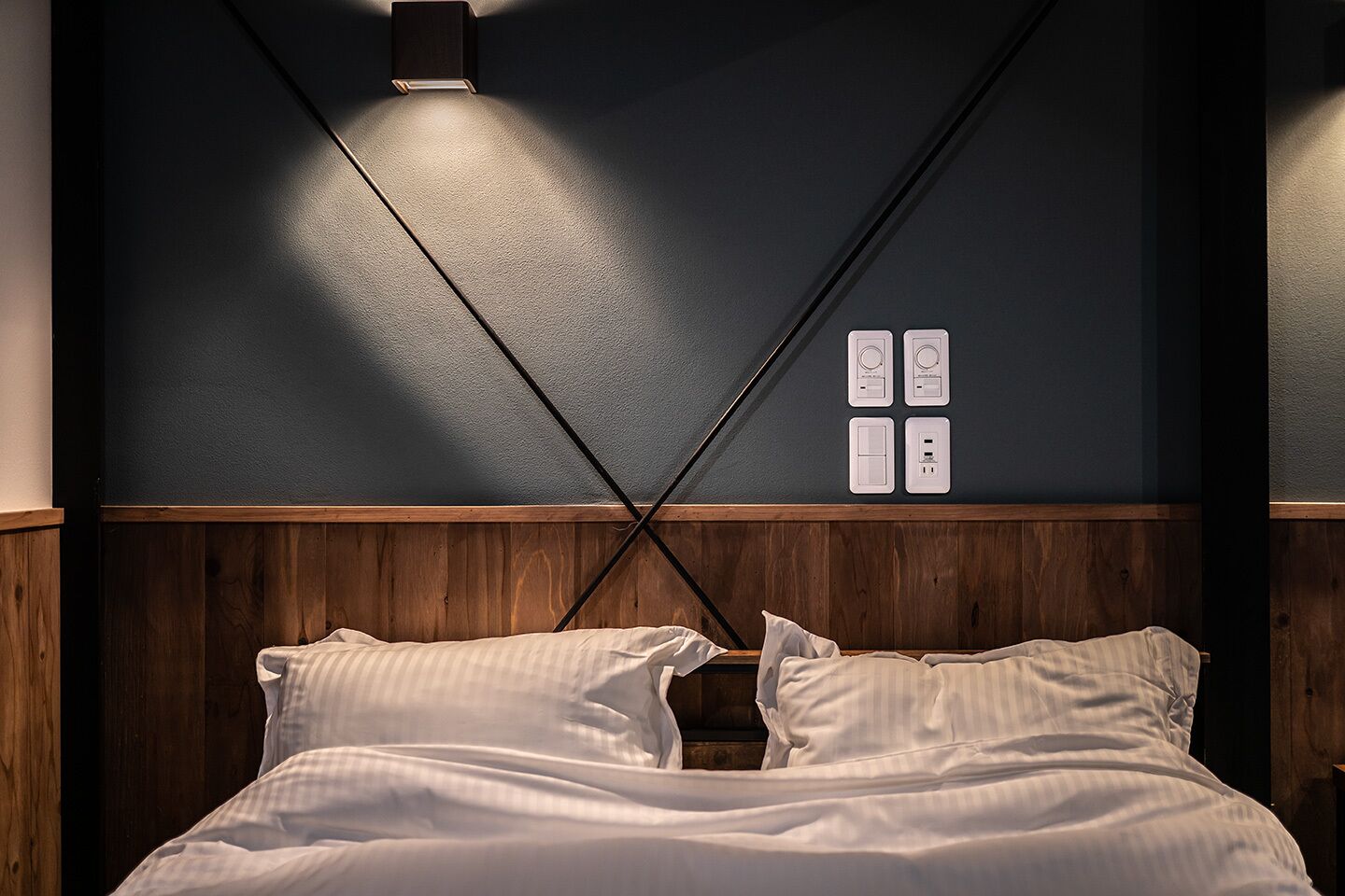 A bedroom with a wooden headboard, a bed with white bedding, and a wall-mounted light fixture.