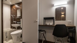Une petite salle de bain comprenant des toilettes, un lavabo et une douche. On y trouve également une chaise et une étagère avec des articles de toilette.