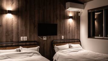 A room with two beds, wooden walls, a mounted TV, and an air conditioning unit.