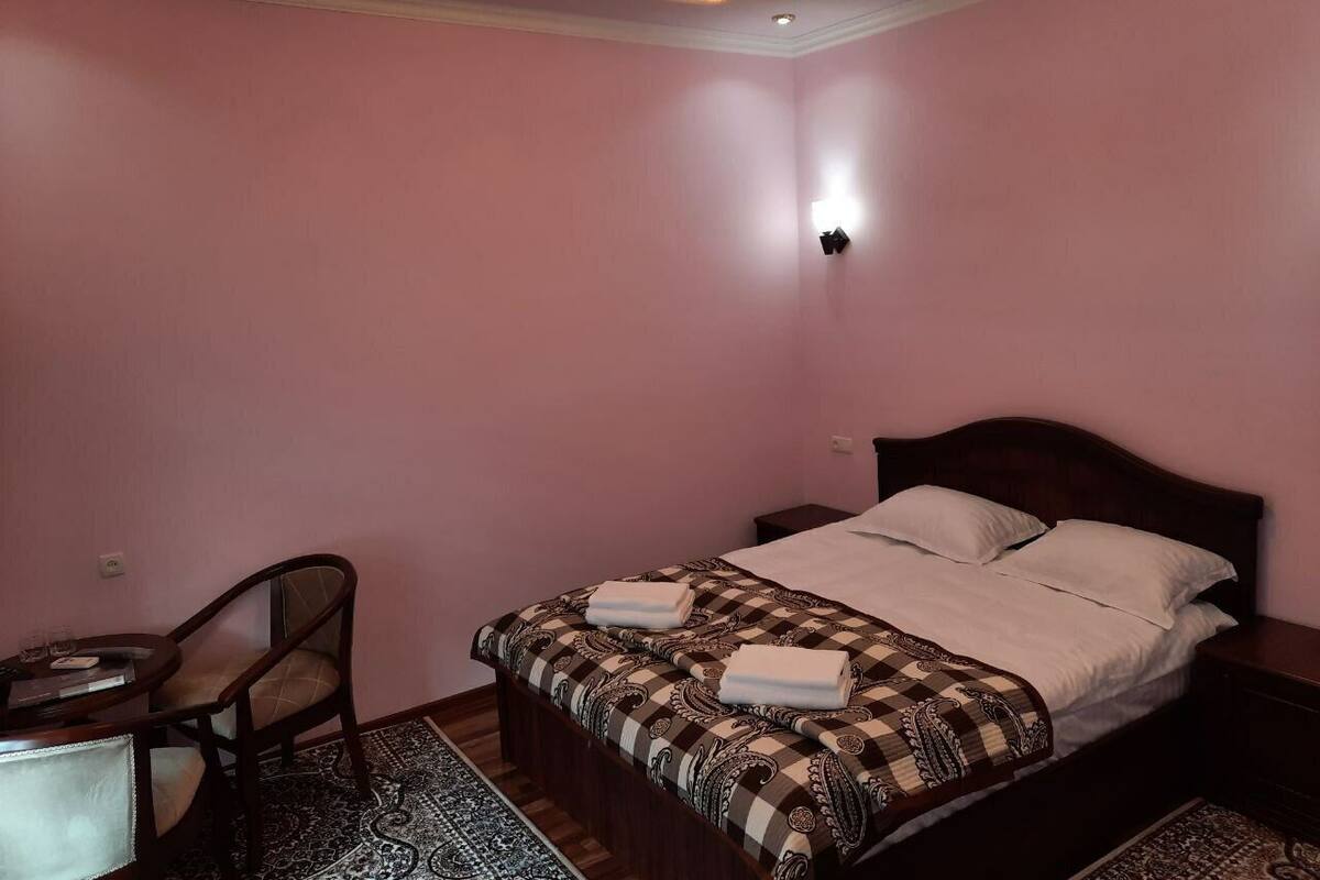 A bedroom with a bed, a chair, a small table, and a wall-mounted light.