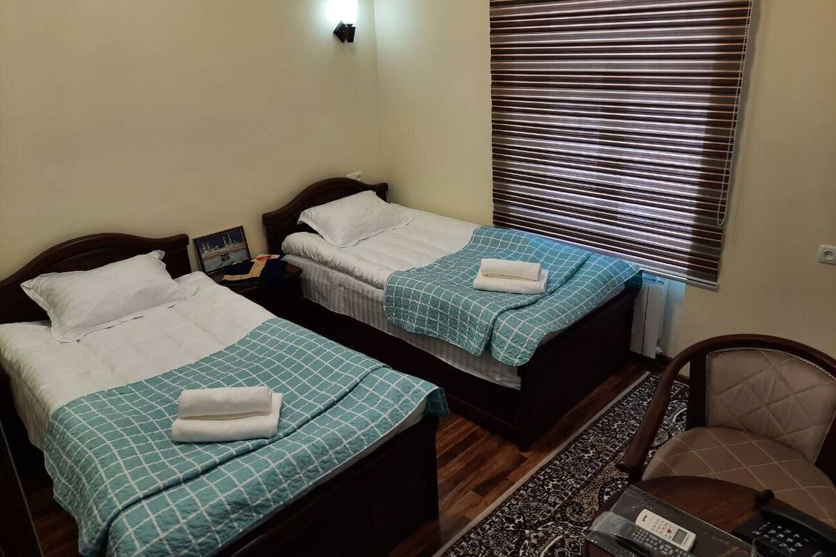 A hotel room with two beds, a chair, a small table, and a window with blinds.