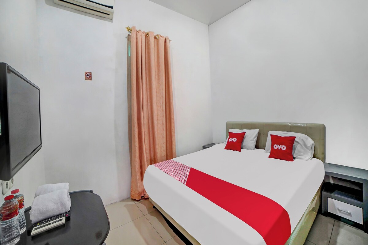 Quarto de hotel com cama, televisão, escrivaninha, garrafa de água e toalha.