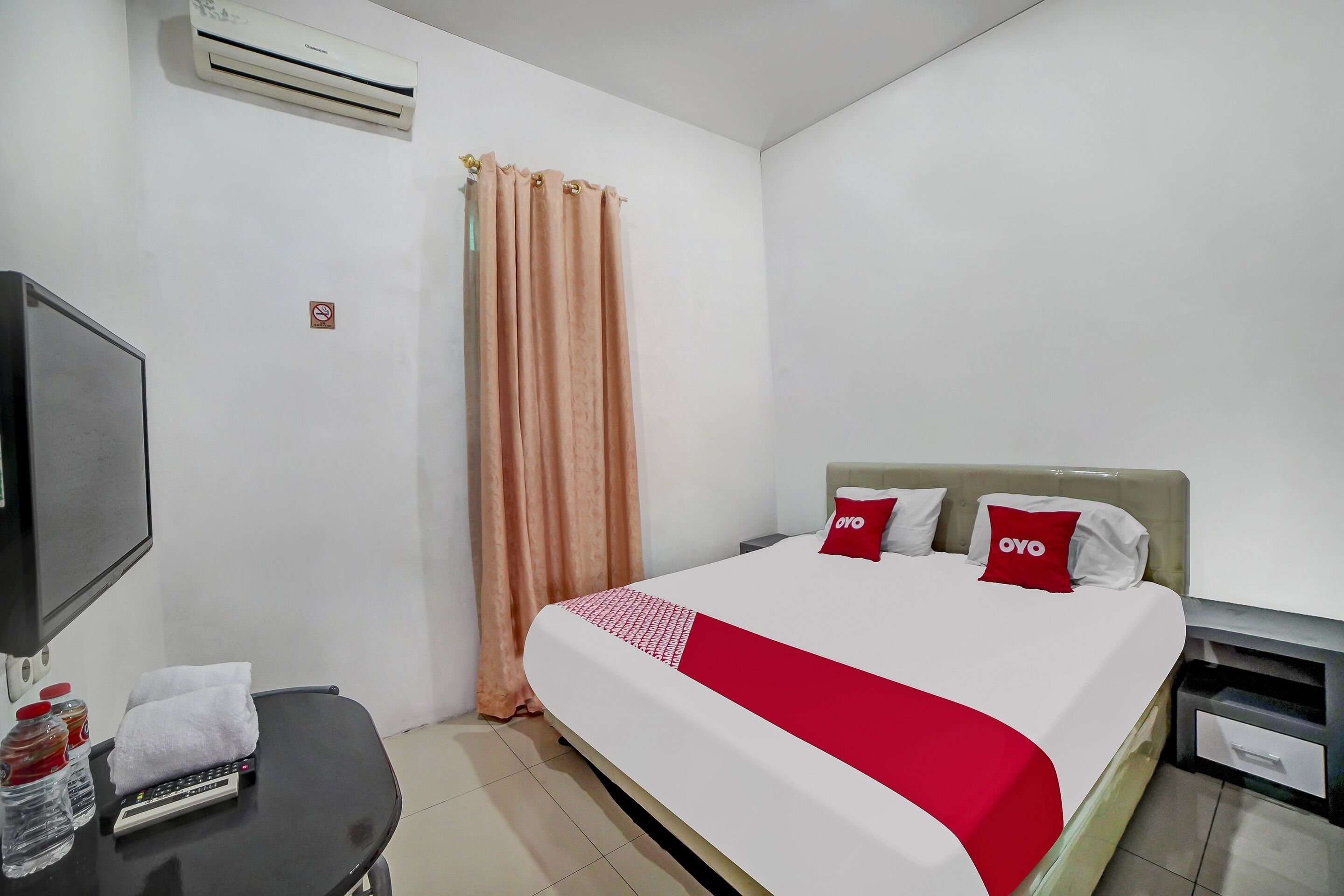 Een hotelkamer met een bed, een televisie, een bureau met afstandsbediening en een gordijn.