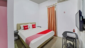 A hotel room with a bed, a TV, an air conditioner, and a small table with a towel and a bottle. - Hotel O Asri Residence (Medan)