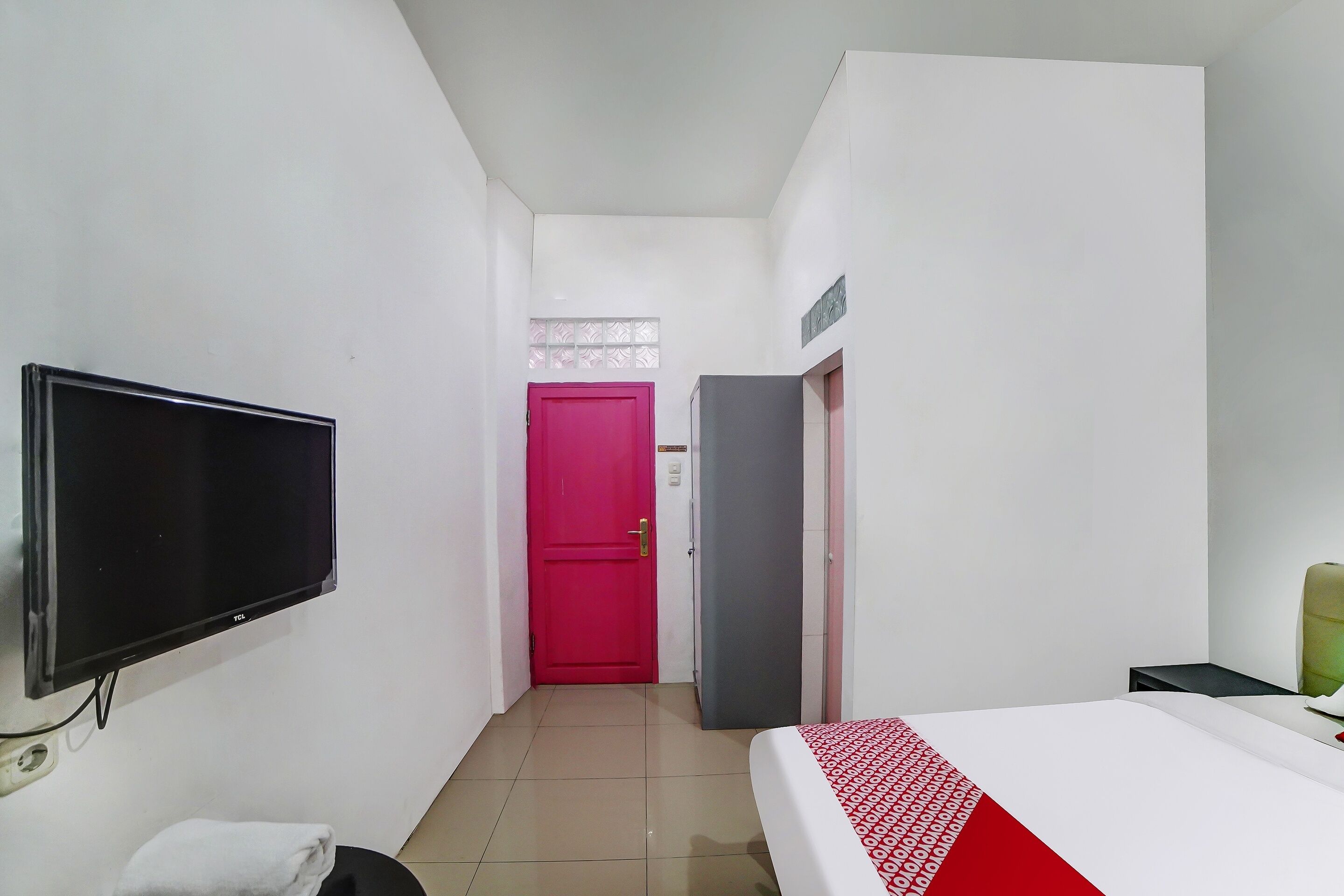 A hotel room with a bed, a television, a red door, and a small table.