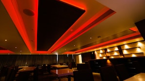 A modern restaurant interior with a dark ceiling, red ambient lighting, and a long dining table with chairs. - Kkm International (Thiruvananthapuram)