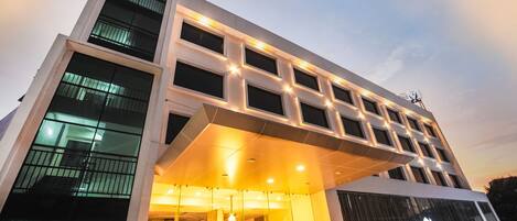 A modern hotel with a prominent glass facade, a covered entrance, and a visible outdoor area with cars.