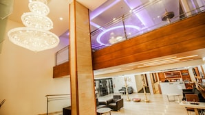 A modern hotel lobby with a chandelier, seating area, reception desk, and a staircase leading to an upper level. - Kkm International (Thiruvananthapuram)