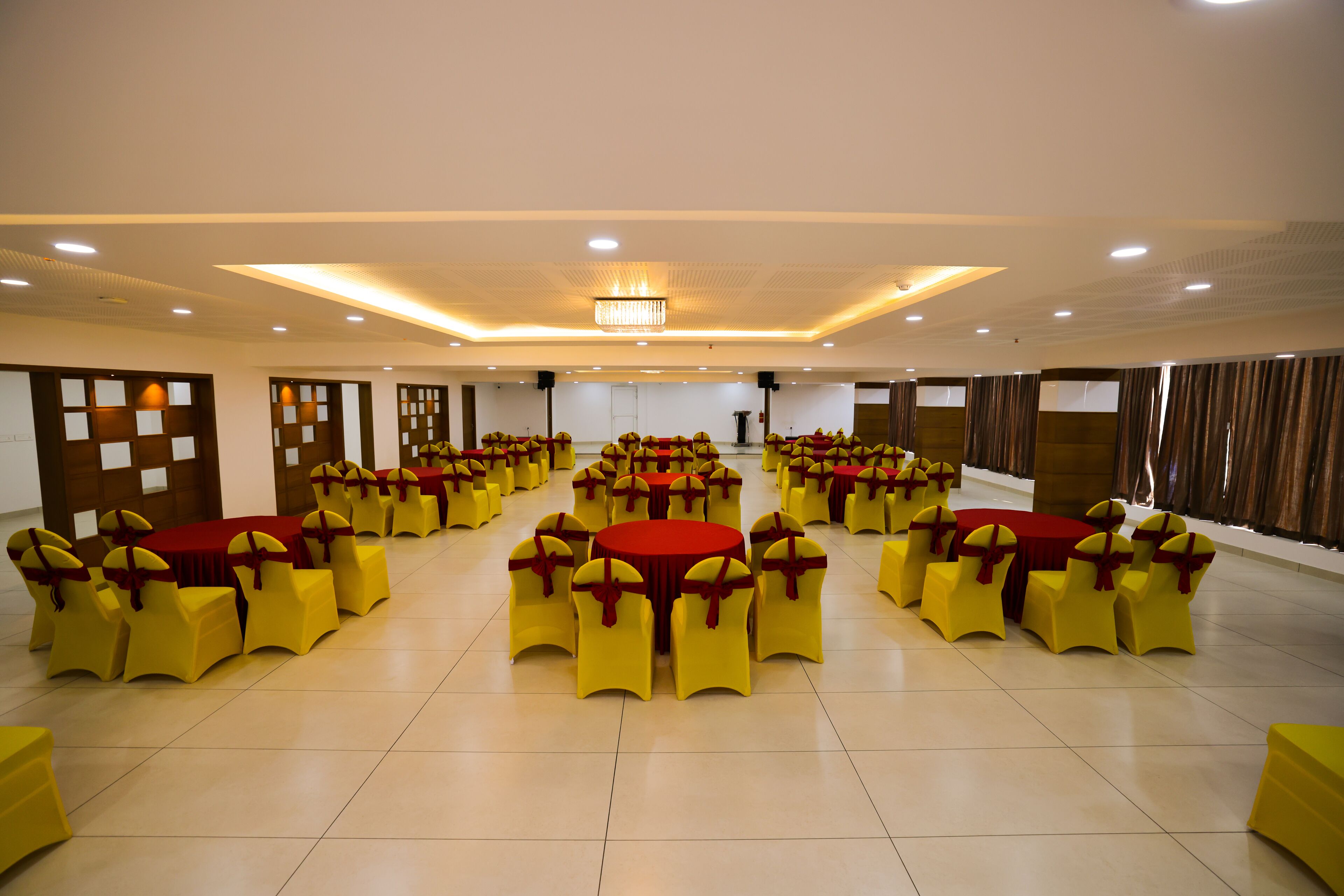 A large hall with multiple round tables and yellow chairs, arranged in rows.