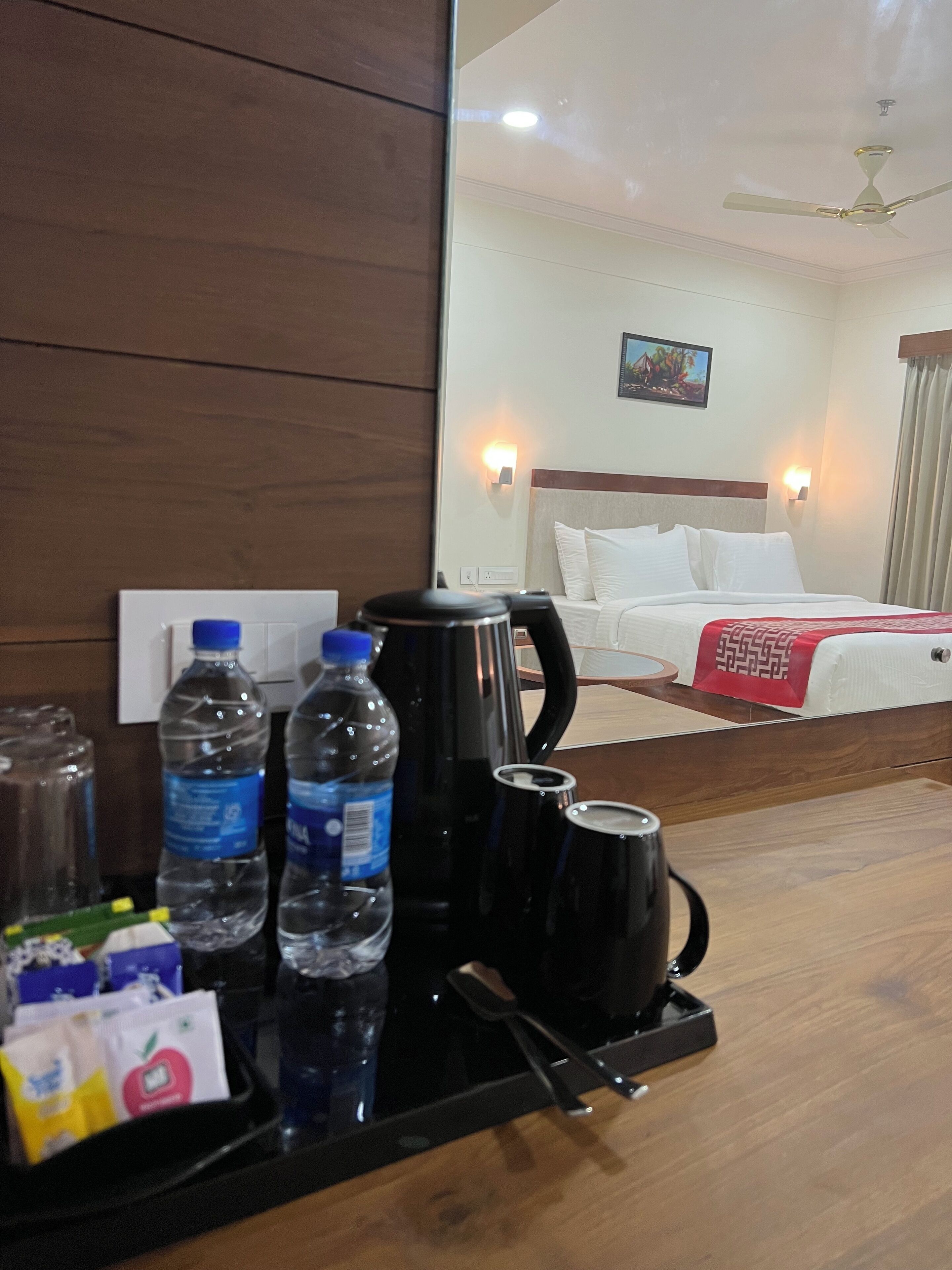 A hotel room with a bed, a nightstand with a coffee maker, water bottles, and a tray with breakfast items.