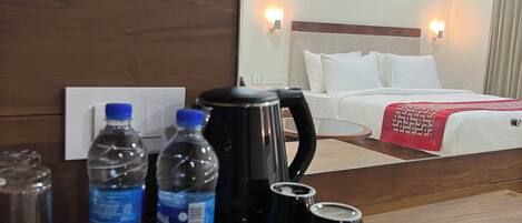 Habitación de hotel con cama, mesita de noche con cafetera, botellas de agua y bandeja con artículos para el desayuno.