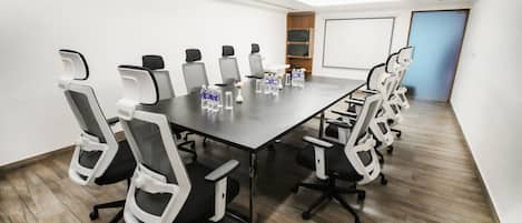 A conference room with a long table, multiple chairs, water bottles, and a projector screen.