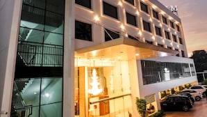 A modern hotel with a glass facade, a staircase leading to the entrance, and a parking area with cars. - Kkm International (Thiruvananthapuram)