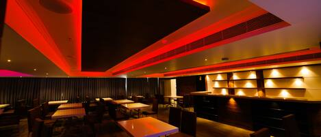 A modern restaurant with a bar area, multiple tables, and chairs arranged for dining.