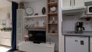 Ein modernes Wohnzimmer mit Flachbildfernseher, einem kleinen Couchtisch und einer Küchenzeile mit Mikrowelle und Kühlschrank.