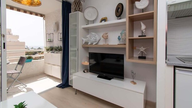 Ein modernes Wohnzimmer mit Flachbildfernseher, weißen Schränken, Dekoration und Blick auf den Balkon.