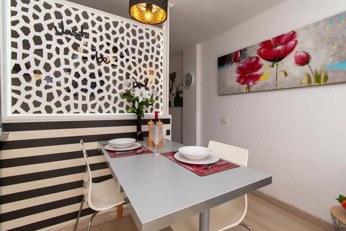 Un coin repas avec un mur à rayures, un élément de séparation décoratif et un tableau représentant des fleurs.