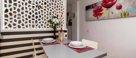 Un coin repas avec un mur à rayures, un élément de séparation décoratif et un tableau représentant des fleurs.