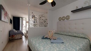 Ein Schlafzimmer mit einem Bett, einem Deckenventilator, einem Fenster mit Vorhängen, einer Couch und einer dekorativen Wandverkleidung.