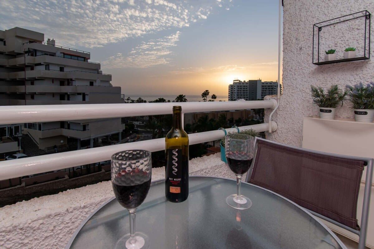 A balcony with a sunset view, two wine glasses, and a bottle of wine.