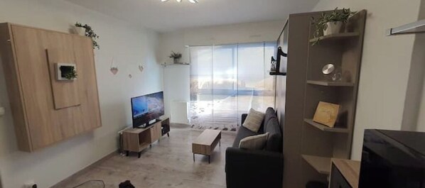 Relax in this stylish living room with a flat-screen TV, comfortable sofa, and sliding glass door leading to an outdoor area.
