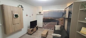 Relax in this stylish living room with a flat-screen TV, comfortable sofa, and a large window offering a view of the surrounding landscape.