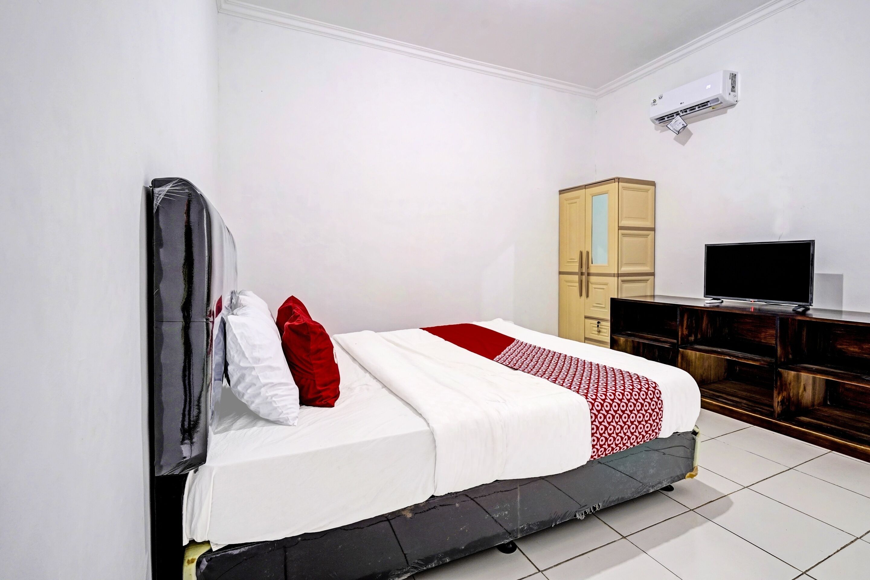 A bedroom with a bed, a television, a wardrobe, and an air conditioning unit.