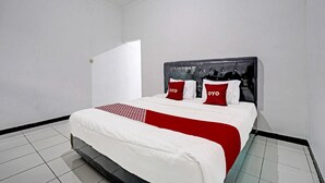 A neatly made bed with a red and white bedspread, a black upholstered headboard, and two red pillows with the word "OYO" on them. - OYO 91334 Permata Papua Guest House (Pameungpeuk)