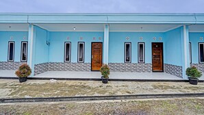 A building with a light blue exterior, multiple doors, and windows. There are two potted plants on the ground. - OYO 91334 Permata Papua Guest House (Pameungpeuk)