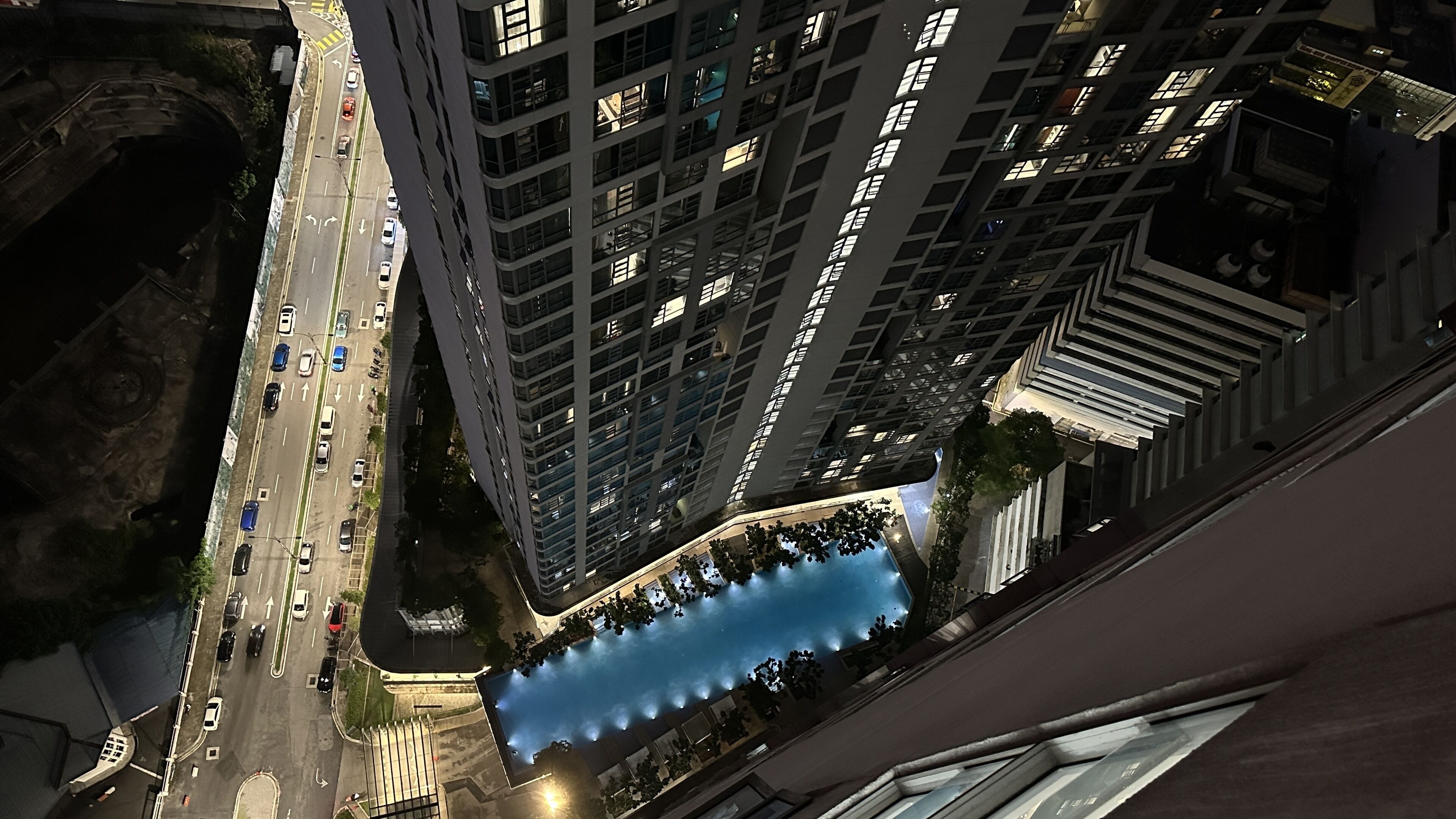 A high-rise building with multiple floors, a parking lot with cars, and a blue water feature in the foreground.