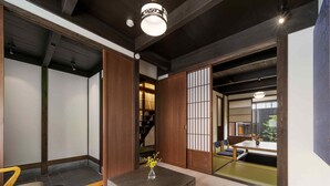 Une pièce de style japonais traditionnel, avec un sol recouvert de tatamis, une basse table en bois ornée d’un vase, des portes coulissantes en papier de riz (shoji) et une vue sur un coin cuisine.