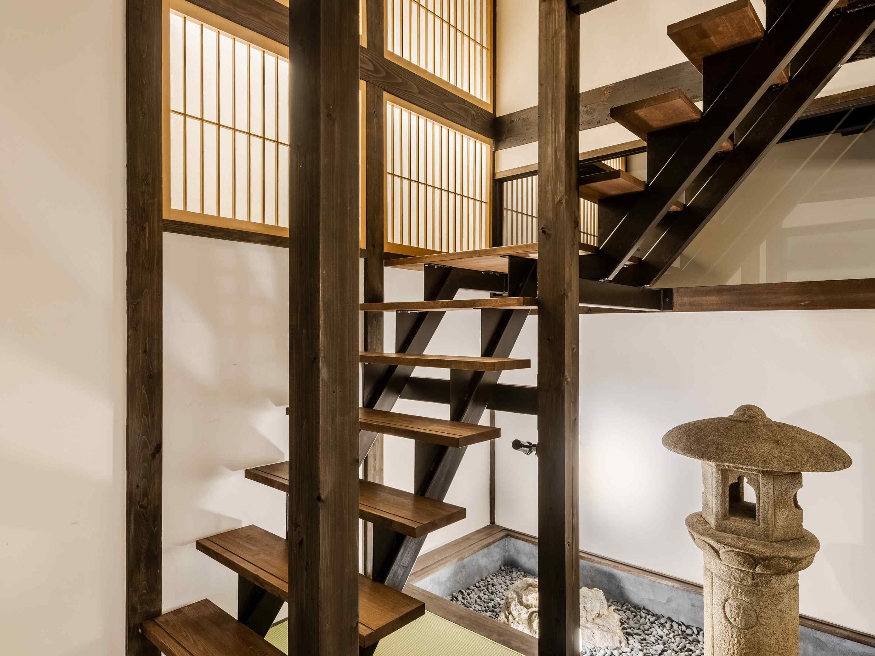 A traditional Japanese-style interior with a wooden staircase, tatami flooring, and a stone lantern.