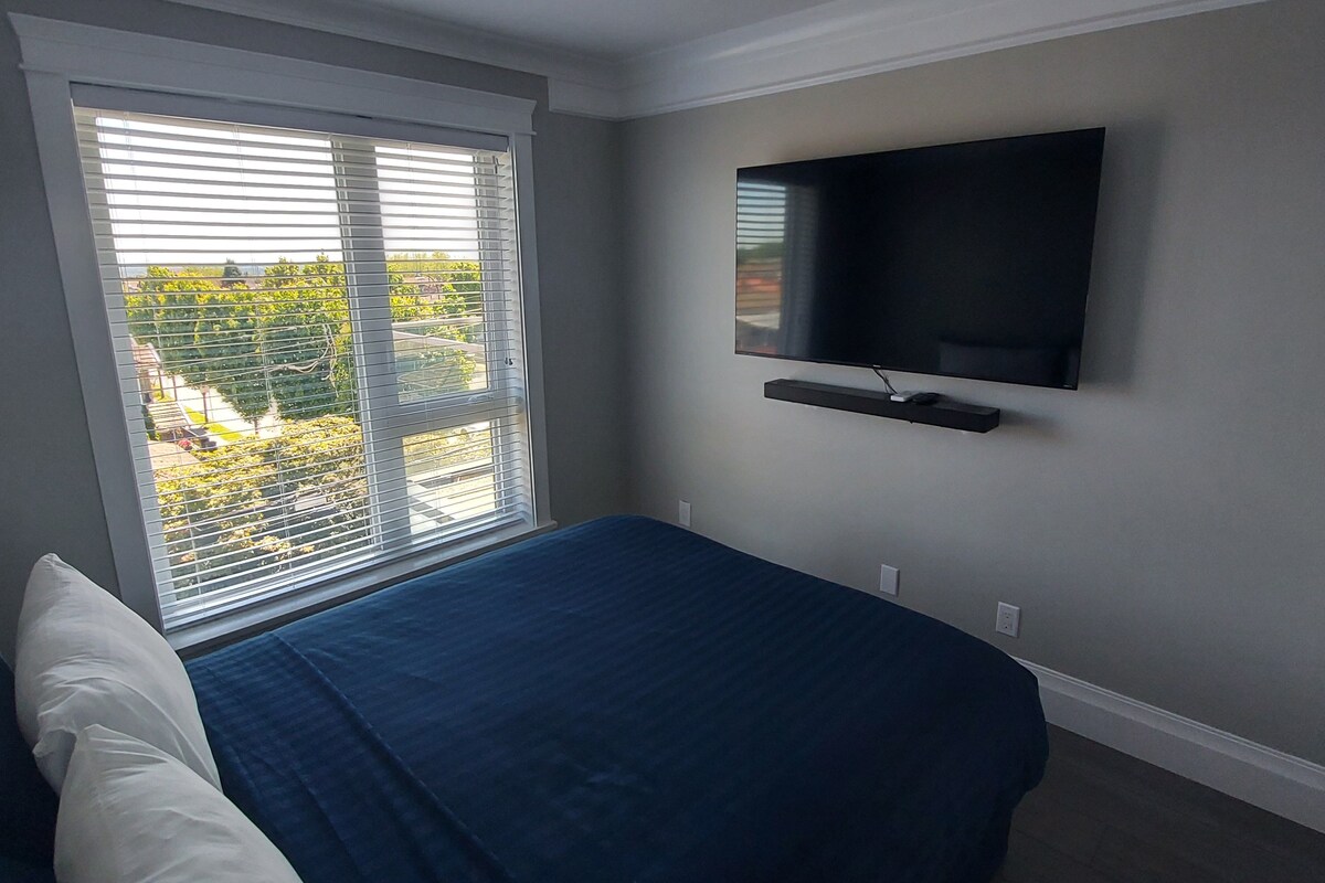 A bedroom with a bed, a TV mounted on the wall, and a window with blinds.