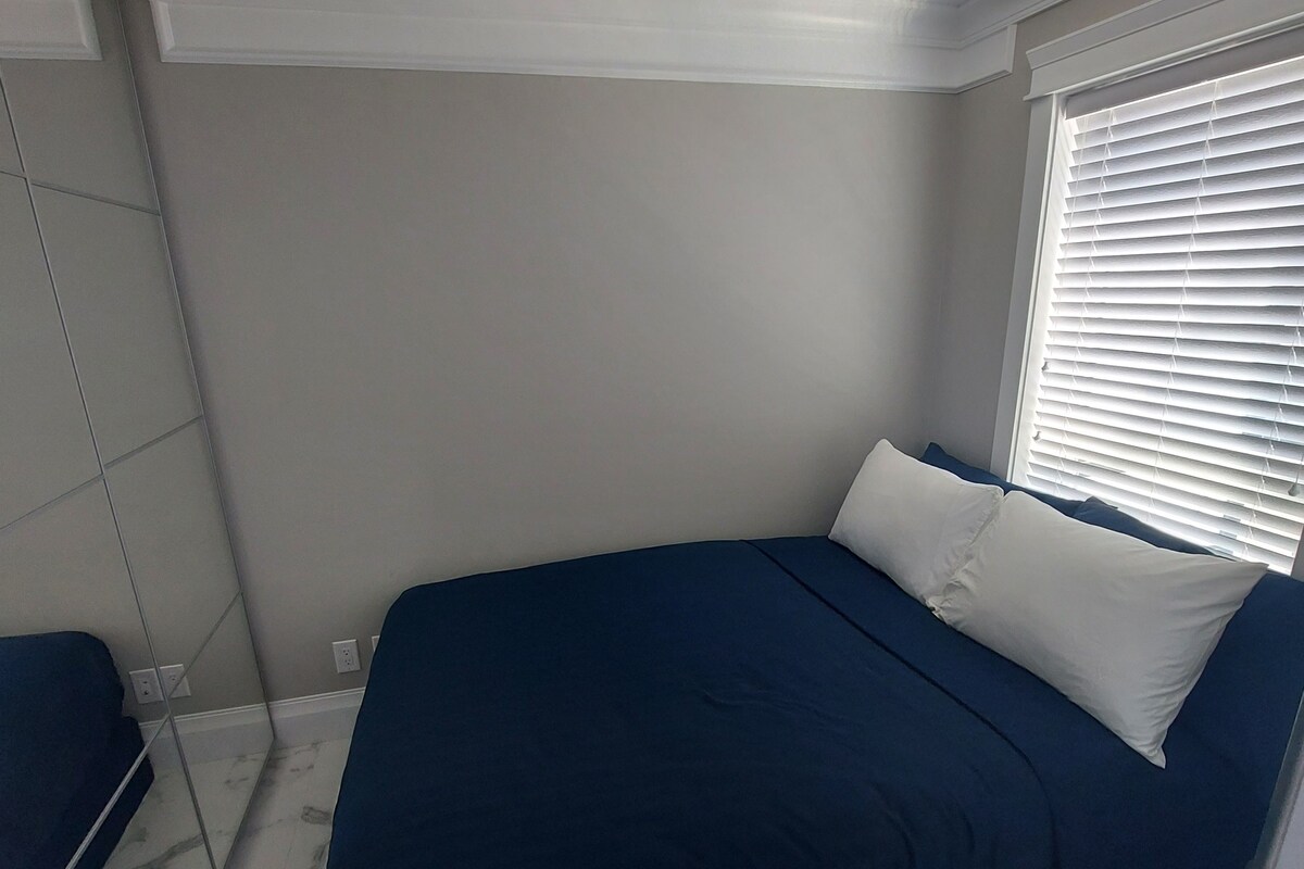 A bedroom with a bed, a window with blinds, and a marble floor.