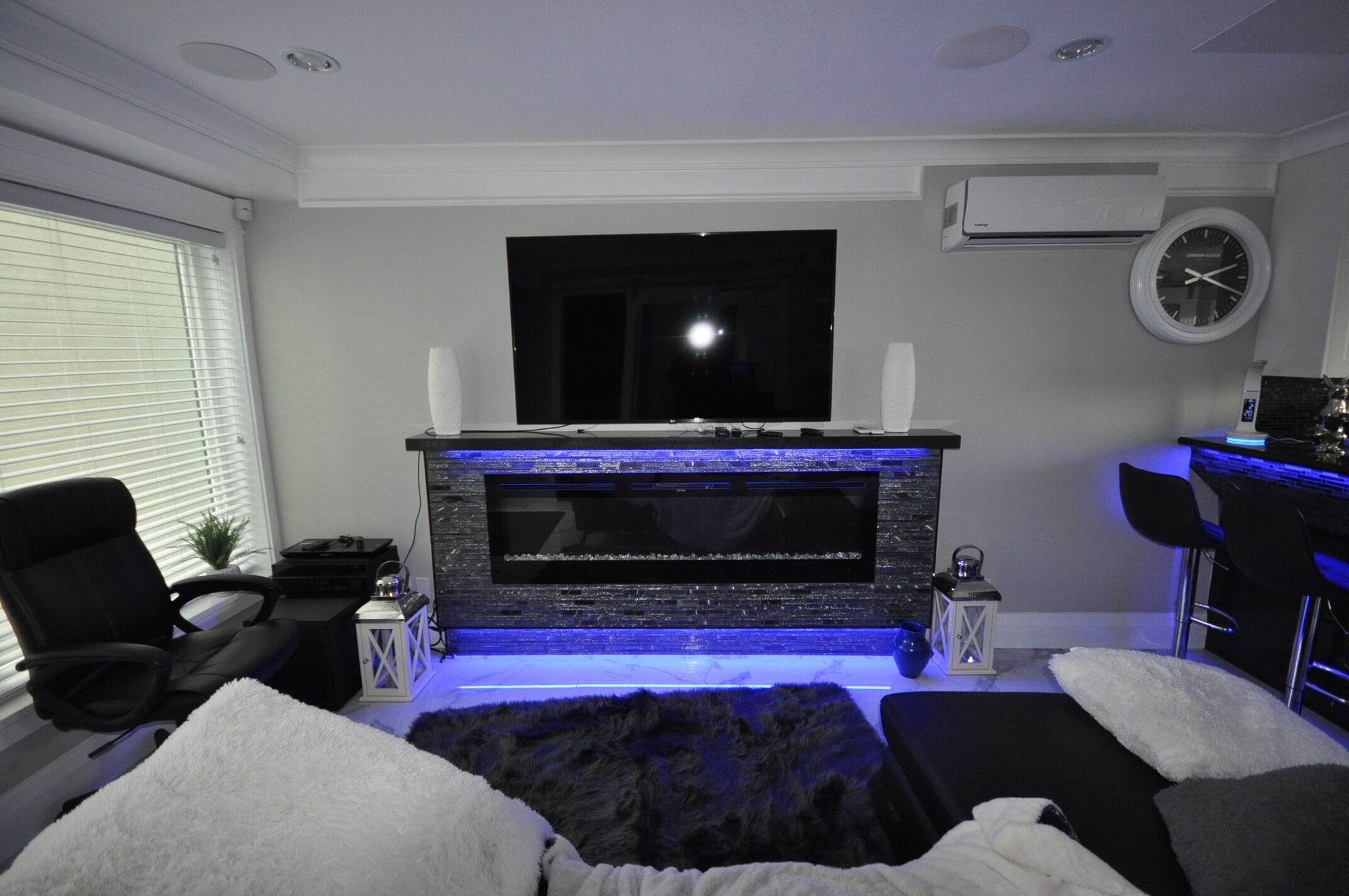 A modern living room with a flat-screen TV mounted above a fireplace, a comfortable seating area with a sofa and chairs, and a small side table with decorative items.