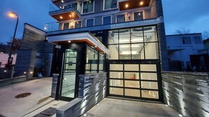 A modern building with a glass facade, a black entrance, and a balcony with lights.