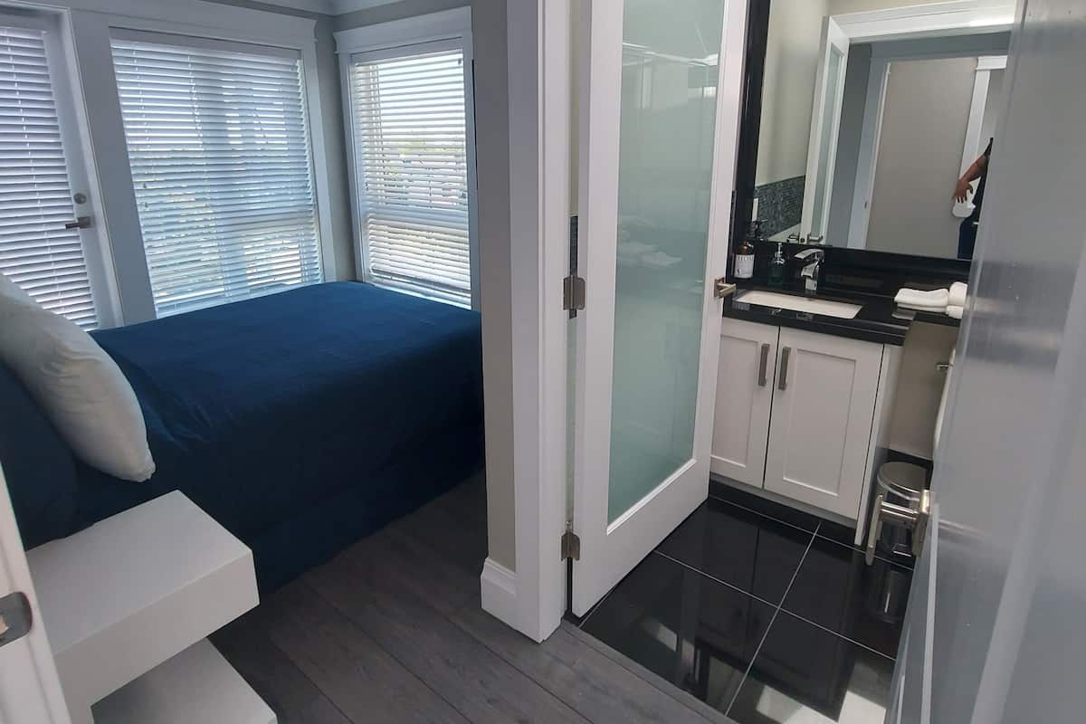 A bedroom with a bed, a bathroom with a mirror and sink, and a door leading to another room.