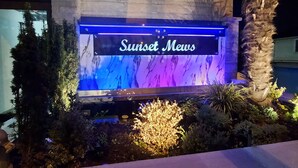 A nighttime view of a building with a sign reading "Sunset Meus" illuminated by blue and purple lights.