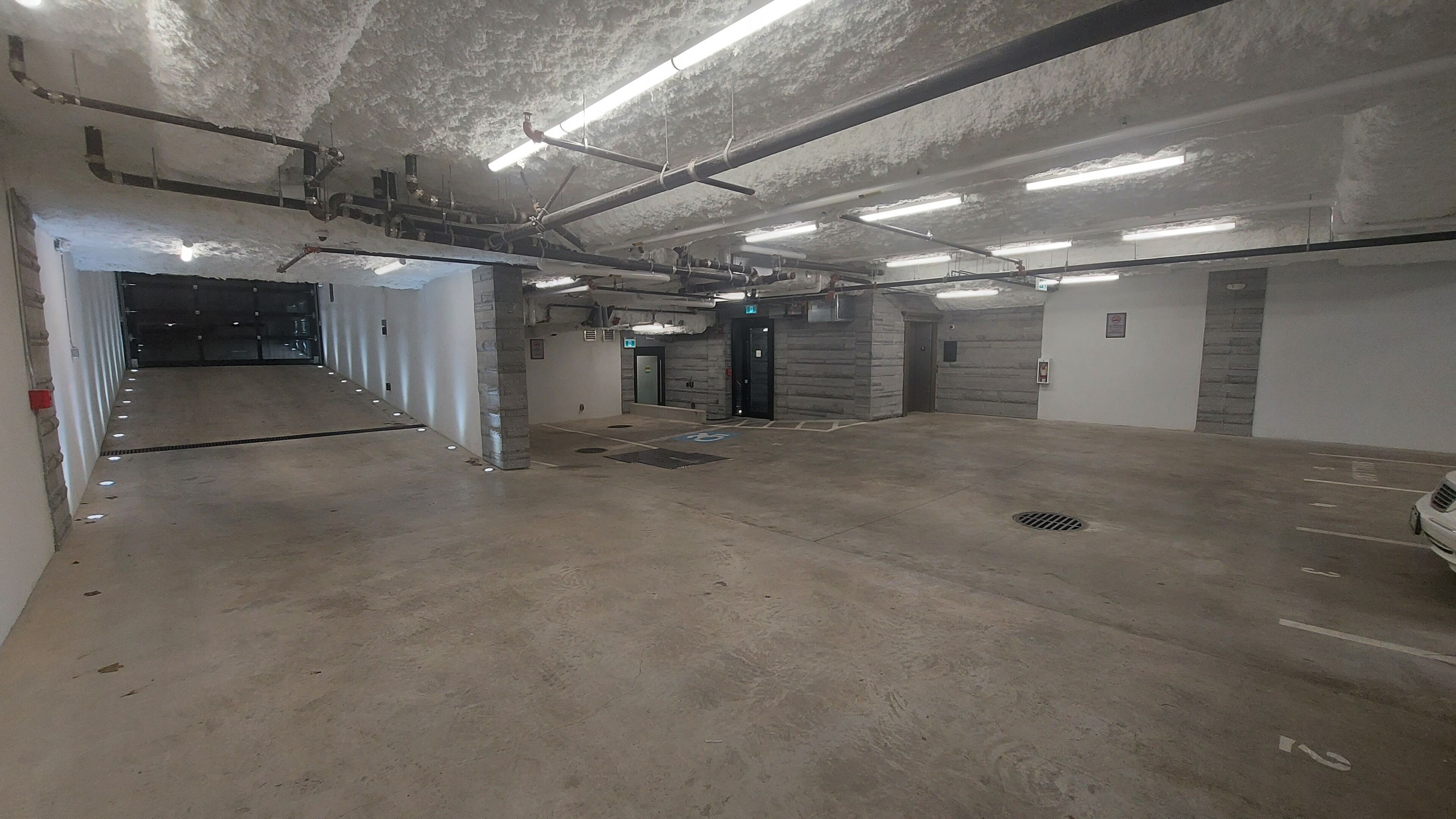 An underground parking garage with concrete floors, multiple parking spaces, and overhead lighting.