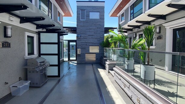 A modern outdoor corridor with a central stone structure, glass railings, and potted plants.