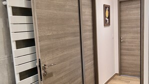 Un pasillo con puerta de madera, radiador blanco y suelo de baldosas.