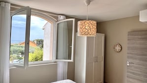 Un dormitorio con cama, armario, puerta, ventana con cortinas y lámpara colgante.