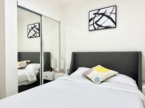 A hotel room with a bed, a nightstand, a lamp, a mirror, and abstract art on the wall. - Lovely 1 bedroom 1B1B in a cozy house (San Jose)