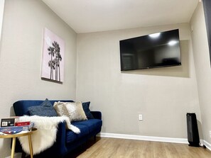 A living room with a blue sofa, a flat-screen TV mounted on the wall, and a small table with a white furry throw. - Lovely 1 bedroom 1B1B in a cozy house (San Jose)