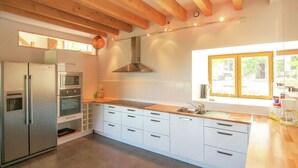 A modern kitchen with wooden beams, stainless steel appliances, and a large window. - Holiday Home in Romefort near Lac de Vassiviere (Saint Léonard de Noblat)