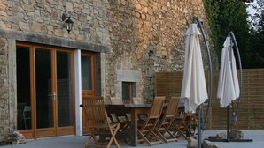 An outdoor patio with a stone wall, wooden table and chairs, and umbrellas. - Holiday Home in Romefort near Lac de Vassiviere (Saint Léonard de Noblat)