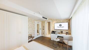 Une chambre d’hôtel avec un grand lit, un bureau, une chaise et un mini-bar. Il y a un miroir au mur et une porte qui donne sur une autre pièce.