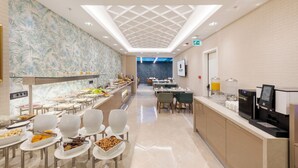 Un moderno vestíbulo de hotel con una larga barra de buffet, zona de estar y un techo con diseño geométrico.