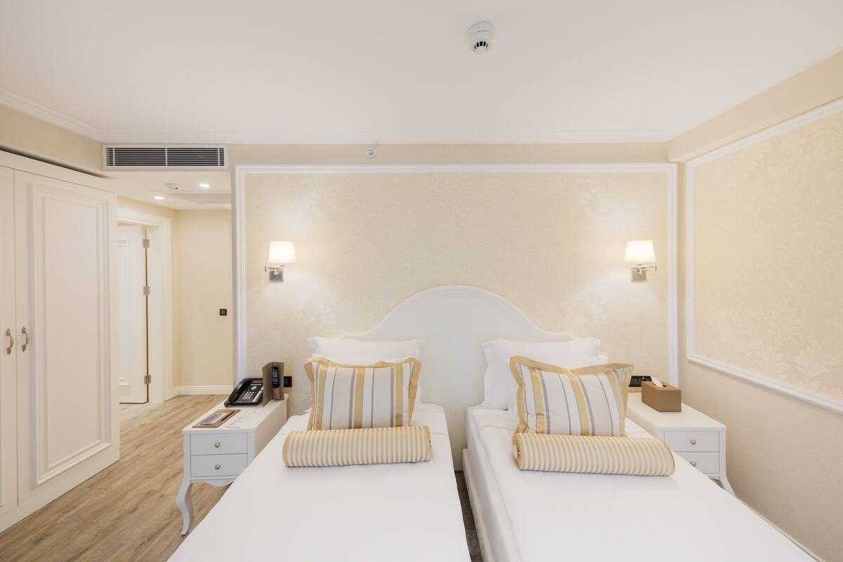 A hotel room with two beds, a bedside table with a lamp, a telephone, and a small bedside table with a tissue box.
